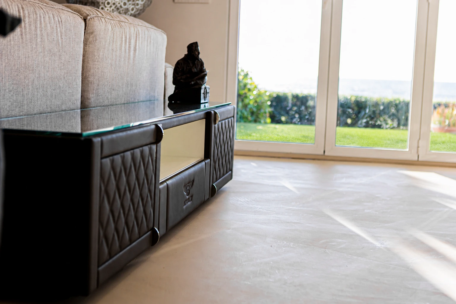 Mueble oscuro junto a un sofá claro y grandes ventanales.